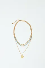 Set de tres collares dorados de diferentes largos. El primero es una cadena de eslabones grandes, el segundo es una cadena con cuentas celestes y una perla, y el tercero es una cadena fina con pequeñas esferas y un dije redondo con textura.