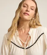 Blusa color crema de tricolina con detalles de ondas negras en cuello, mangas y frente. Tiene mangas 3/4 con volados y lazo en el cuello.