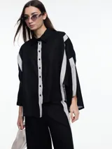 Camisa de lino color negro con silueta amplia y mangas 3/4. Diseño con tiras de color blanco en contraste en la cartera, mangas y cuerpo. Tiene tajos laterales y ruedo irregular en el frente.