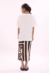 Remera blanca de algodón, corte oversize, con cuello redondo y manga corta. Presenta un estampado frontal con varias reposeras y hamacas de playa, y el texto "LA SIESTA".