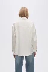 Camisa color crudo de viscosa, corte holgado, con cuello camisero, cierre frontal con botones, manga larga y dos bolsillos con solapa en el pecho.