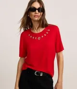 Remera de viscosa color rojo, corte clásico, con cuello redondo y mangas cortas. Presenta aplicación de strass en el escote.