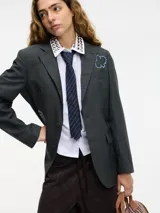 Blazer gris oscuro de lana con cuello solapa y cierre con botones. Presenta pedrería decorativa en la parte delantera y trasera.