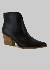 Botín de cuero negro con punta fina, caña baja con corte en V y cierre trasero con cremallera. Tiene un taco de madera con forma geométrica.