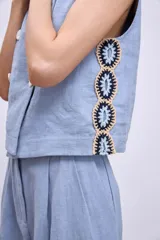 Chaleco celeste con diseño cruzado y doble botonadura, sin mangas y con apliques de encaje en los laterales.