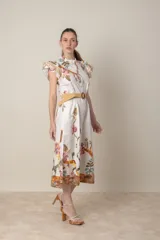 Vestido midi camisero de algodón color natural con estampado de flores, animales y ramas en tonos rojo, marrón, verde y azul. Tiene cuello mao, mangas cortas con volados, bolsillos laterales y cinturón de soga color beige.