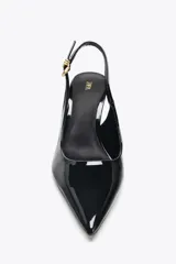 Zapato de tacón destalonado color negro charol, con punta fina y tira trasera con hebilla metálica dorada.