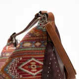 Bolso tipo hobo con estampado geométrico multicolor y detalles de tachas en los bordes.