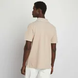 Remera polo color beige de piqué de algodón, con cuello clásico con borde blanco, tapeta de dos botones y mangas cortas con borde blanco.