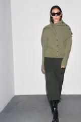 Chaqueta de punto color rosa pálido, con cuello redondo y cierre frontal de botones oscuros. Presenta mangas largas y un corte a la cintura.