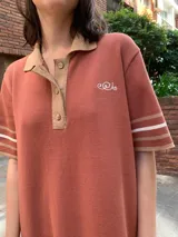 Vestido color ladrillo de tejido de hilo, corte recto, cuello polo con botones y mangas cortas con ribete en color beige.