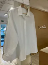 Camisa blanca de lurex con cuello clásico, cierre frontal con botones y mangas largas.