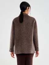 Chaqueta de lana con textura afelpada, color marrón jaspeado. Diseño cruzado con doble botonadura de botones oscuros, solapa clásica y bolsillos con tapa. Corte recto y ligeramente oversize.