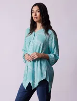 Blusa celeste con estampado de cachemir en blanco, cuello a la base, escote en V y abertura central con botones. Manga 3/4 regulable con presilla y botón, y terminación de ruedo asimétrico.
