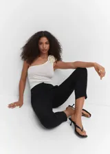 Pantalón negro de corte skinny y largo cropped, confeccionado en tejido fluido con forro interior. Presenta tiro medio, trabillas, bolsillos laterales y traseros de ribete. Cierre frontal con cremallera y botón.