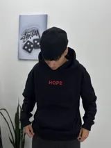 Buzo negro con capucha y bolsillo tipo canguro, con la palabra "HOPE" bordada en rojo en el pecho. Corte oversize.