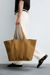 Bolso tipo shopper color marrón claro, fabricado en piel serraje. Cuenta con dos asas de mano y un bolsillo interior con cierre de cremallera.