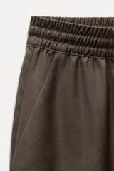 Pantalón de tiro medio color marrón, con cintura elástica ajustable con cordones, bolsillos delanteros y traseros, raya planchada y pierna recta.
