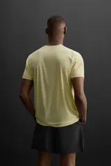 Camiseta deportiva color amarillo claro confeccionada en tejido técnico ligero y elástico. Cuenta con cuello redondo, manga corta, costuras termofijadas y estampaciones reflectantes en la espalda.