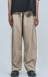 Pantalón deportivo beige de nylon con cintura elástica ajustable con cordón, corte amplio y aberturas laterales con broches.