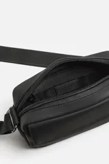 Bandolera negra de acabado engomado, con compartimento principal con cierre de cremallera y bolsillo interior de rejilla con cremallera. Bolsillo frontal con solapa y botones a presión. Asa de hombro ajustable y extraíble.