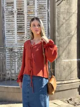 Blusa color terracota de muselina con escote en V y lazos para ajustar. Tiene mangas largas abullonadas con volados en los puños.