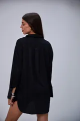 Camisa negra de manga larga, con cuello clásico y cierre frontal de botones blancos.