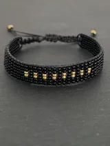 Pulsera tejida con cuentas MIYUKI en tonos de negro y dorado, ajustable con cordón negro.