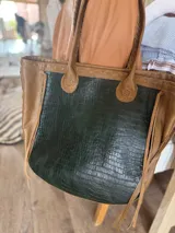 Bolso tipo tote bag con paneles laterales color cuero y panel central con textura de piel de cocodrilo color verde oscuro. Tiene doble asa de hombro color cuero y flecos laterales.
