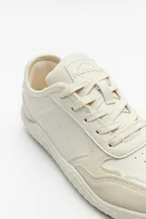 Zapatillas de cuero color blanco y beige, de diseño minimalista con suela marrón.