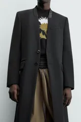 Levita negra de corte relajado confeccionada en tejido con lana. Presenta cuello sin solapa, mangas largas con puños abotonados, bolsillo de vivo en el pecho y bolsillos con solapa en la cadera. Incluye bolsillos interiores, abertura en el centro de la espalda y cierre frontal con botonadura.