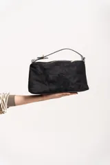 Cartera tipo baguette o clutch de material similar a la gamuza, color negro, con cierre superior y correa corta de mano. Incluye correa larga ajustable para llevar al hombro o cruzada.