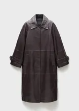 Abrigo largo oversize de cuero ovino color marrón oscuro, con cuello camisero, cierre frontal oculto con cremallera, mangas largas con puños abotonados, forro interior y dos bolsillos laterales.