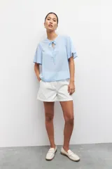 Blusa celeste a rayas verticales con cuello mao, mangas cortas y lazo en el frente.