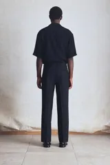 Pantalón de vestir negro de corte recto, confeccionado en mezcla de lino y algodón. Cuenta con cierre frontal con botón y gancho ocultos, bolsillos laterales y traseros ribeteados, pinzas y pliegues delanteros y traseros.