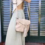 Bandolera color beige con tapa y broche magnético, apertura superior con cierre, detalle de trenzas artesanales y pompones en el frente, correa larga regulable y bolsillos internos.