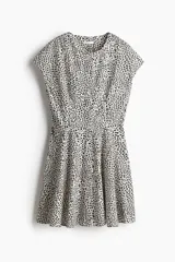 Vestido corto de algodón con estampado de manchas negras sobre fondo blanco. Tiene cuello redondo, mangas cortas tipo japonesa, botonadura frontal y cintura entallada con pinzas. La falda es acampanada con inserciones para dar volumen.