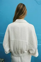Camisa blanca de manga corta con cuello solapa, bolsillos frontales con tapeta, bajo con elástico y cierre frontal con botones a presión.