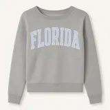 Sweater gris de corte clásico con cuello redondo y puños y cintura acanalados. Estampado frontal con la palabra "Florida" en letras celestes con borde blanco.