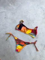 Conjunto de bikini con estampado geométrico multicolor, compuesto por un corpiño bandeau con breteles regulables y una bombacha vedetina con tiras laterales para atar.