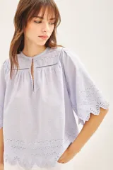 Camisa celeste de algodón con bordado inglés, corte amplio, cuello redondo y mangas cortas con terminación festoneada.