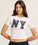 Remera de algodón color crudo, corte new t-shirt ajustado al cuerpo, con cuello redondo y manga corta. Estampa frontal con las letras 'NY' en azul con efecto desgastado.