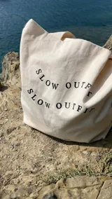 Tote bag color crudo con estampa negra con la frase "Slow Outfit" repetida.