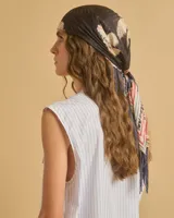 Pañuelo de seda negro con estampado floral en tonos beige y flecos en los extremos.