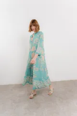 Vestido largo azul con estampado floral en tonos beige, confeccionado en viscosa. Presenta escote en V, botonadura completa en el frente y mangas largas con volados.