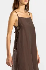 Vestido largo color marrón chocolate, con breteles finos y escote recto. Presenta lazos en los costados, forro hasta arriba de las rodillas y caída posterior más larga.