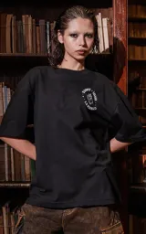 Remera negra de manga corta con cuello redondo y calce oversize. Presenta una estampa en la espalda inspirada en el tarot, con la carta "La Fuerza" que muestra a una mujer desnuda sobre un leopardo, rodeada de vegetación y un sol rojo.