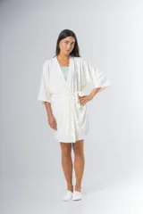 Bata tipo kimono de algodón color blanco hueso, con textura acanalada vertical. Presenta un cruce frontal asegurado con un lazo a la cintura y mangas anchas de largo al codo.