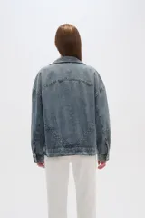 Campera de jean celeste con cuello clásico, solapas, cierre frontal con botones metálicos y mangas largas con puños abotonados. Presenta detalles de costuras diagonales y apliques de tachas metálicas.