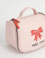 Neceser de viaje color rosa con cierre superior y manija. Estampado frontal con un moño rojo con corazones y la frase "Très Chic".